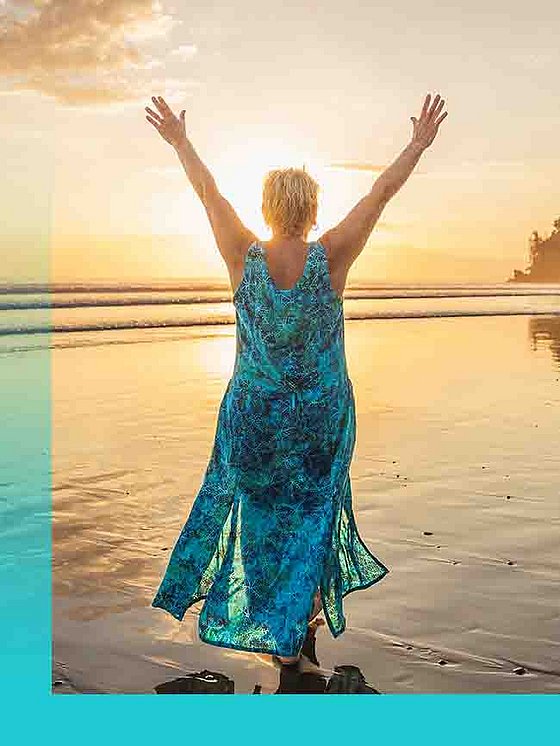 Eine Frau in türkisenem Sommerkleid von hinten läuft am Strand bei Sonnenuntergang