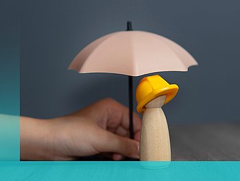 Eine Hand hält einen Holzmenschen mit gelbem Helm und Regenschirm